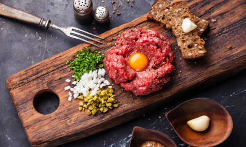 Beef tartare with pickled cucumber and fresh onions on dark marble background